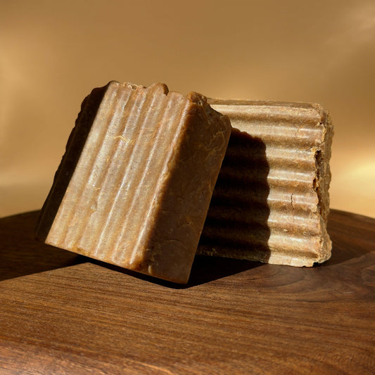 Two brown soap bars with a ribbed texture on a wooden surface.