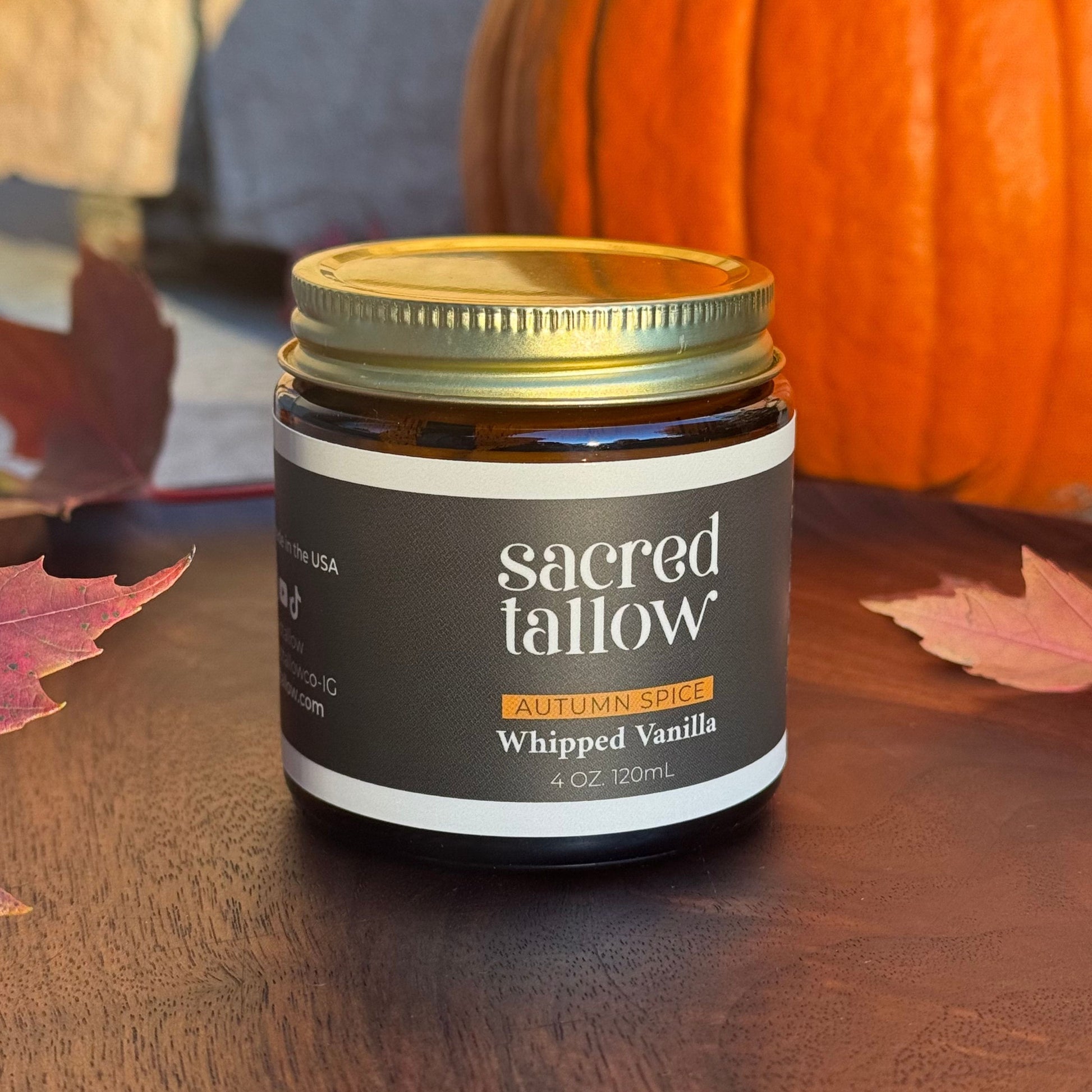 Jar of 'sacred tallow' whipped vanilla on a wooden surface with pumpkins and leaves in the background