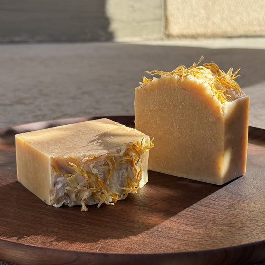 Two bars of soap with visible herbs on a wooden surface