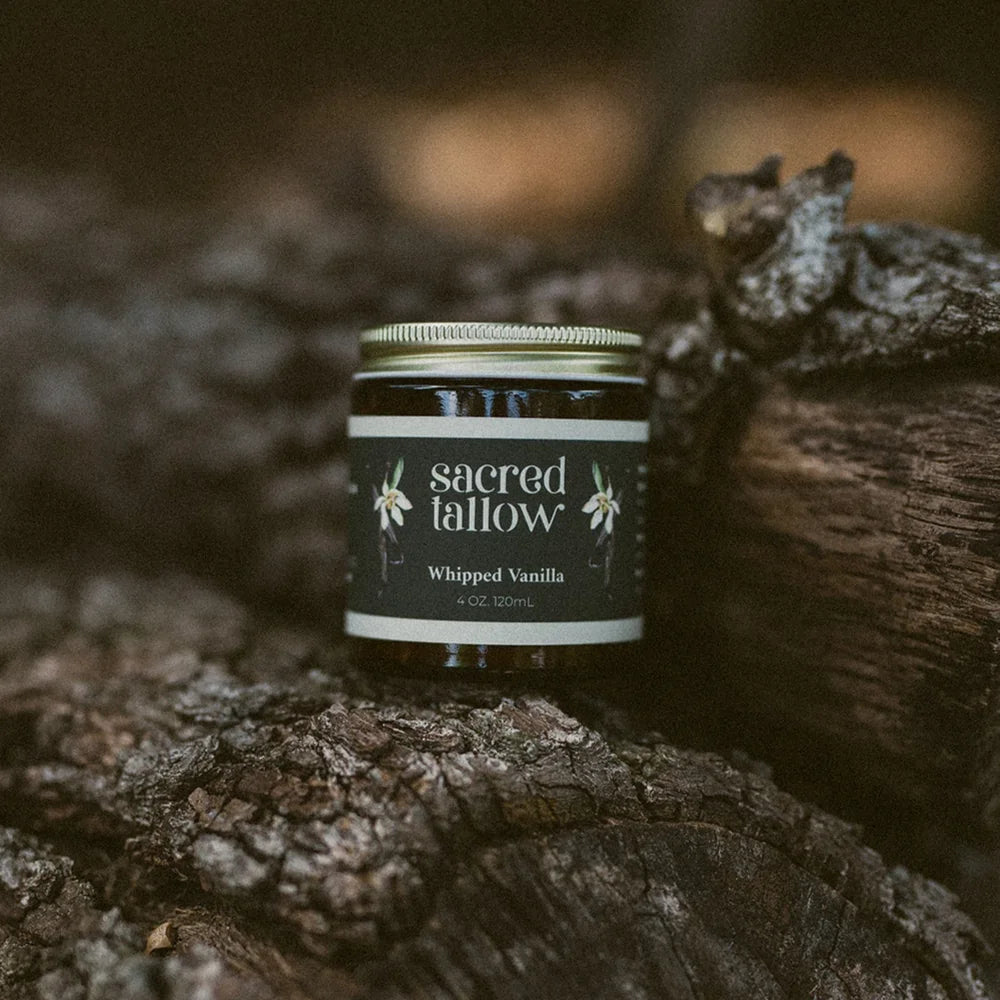 A small jar of Sacred Fallow Whipped Vanilla candle placed on textured tree bark in a natural outdoor setting.