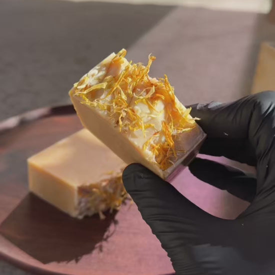 Two bars of soap with visible herbs on a wooden surface