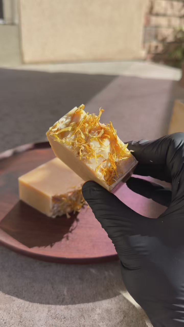 Two bars of soap with visible herbs on a wooden surface