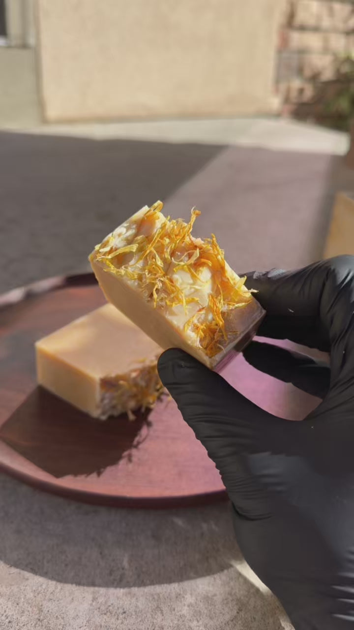 Two bars of soap with visible herbs on a wooden surface